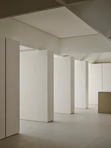 Minimalist interior space featuring multiple white vertical volumes, micro-cement floors, and dramatic geometric ceiling with hidden lighting.