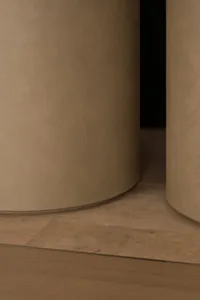 Close-up architectural detail showing a curved micro-cement wall in warm beige tones meeting a light oak wood floor with a thin metal transition strip.