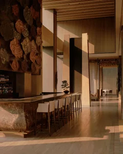 Luxurious long marble bar with white leather bar stools in a high-end lounge featuring a massive traditional Chinese cloud pattern wall carving and warm ambient lighting.