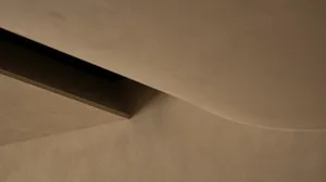 Close-up architectural detail showing a curved micro-cement surface meeting a flat plaster wall with a deep recessed shadow gap.