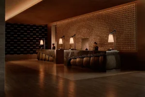 Luxurious hotel reception desk featuring a large feature wall covered in circular wooden discs, dark stone counter, and warm pendant lighting.