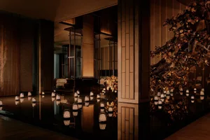 奢華日式餐廳室內設計，淺水倒影池旁排列著發光編織燈籠，深色木質建築與大型金葉雕塑樹相互輝映。