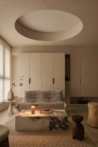 Minimalist living room featuring a large Calacatta marble coffee table, a modular beige sofa, textured boucle rug, and a dramatic circular recessed ceiling light.