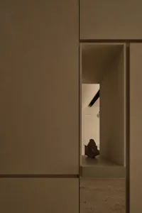 Close-up view of a minimalist micro-cement niche shelf displaying a dark sculptural rock against warm beige walls in an earthy modern interior.