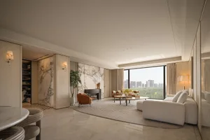Modern luxury living room featuring large marble feature wall, white sectional sofa, burnt orange accent chair, and floor-to-ceiling windows overlooking a city skyline.