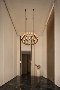 Modern luxury hallway with black marble floor, white textured walls, large contemporary chandelier, and abstract sculpture on a marble pedestal.
