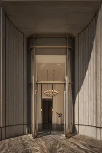 View from inside a luxurious building entrance looking through open ornate brass and glass doors into a grand lobby with a large chandelier, dark marble floor and travertine walls.