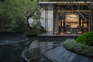 Modern luxury courtyard at dusk featuring a dark marble reflecting pool with flowing water, teak lounge chairs on a raised pavilion, and lush green landscaping with trees and shrubs.