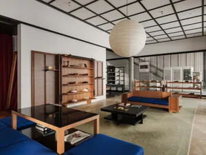 Modern shoe store interior with teak wood shelving, blue sofas, black coffee tables, and a large white paper lantern pendant light.