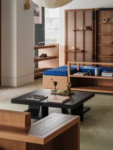 Modern living room interior with light oak built-in cabinetry, a low black coffee table on a textured rug, royal blue daybed cushions, wooden shoji-style screens, and a large paper lantern pendant.