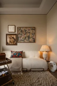 Cream-colored textured sofa with floral pillow, layered gallery wall art, table lamp, and shaggy beige rug in a warm living room corner