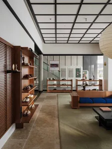 Modern minimalist shoe store interior featuring walnut wood display shelves, blue cushion seating on a wooden platform, tatami-style rug, large paper lantern, and black grid ceiling.