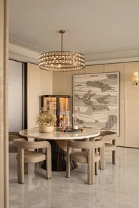 Elegant contemporary dining room with a round Calacatta marble table, fluted beige leather chairs, a large crystal chandelier, and abstract wall art.