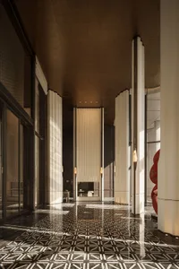 Luxurious Art Deco hotel lobby hallway featuring dramatic black and white geometric patterned marble flooring, tall fluted columns with integrated lighting, and warm metallic ceiling details.