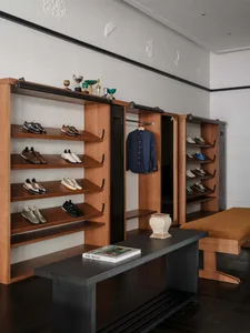 Modern walk-in closet with walnut open shelving displaying numerous sneakers, a navy shirt hanging, dark console table, and upholstered bench in a luxurious dressing room.