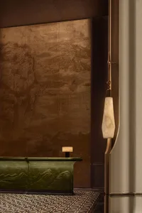 Luxury hotel reception desk in dark green verdigris bronze with carved mountain relief, set against a large bronze-toned Chinese landscape mural, with marble pendant light and geometric patterned carpet.