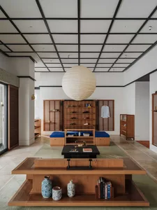 Modern Japanese-style living room featuring a large walnut low table, blue floor cushions, built-in wooden storage, and a large white paper lantern hanging from a grid ceiling.