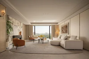 Modern luxury living room featuring a large curved off-white sectional sofa, burnt orange bouclé armchair, marble accent wall with fireplace, and floor-to-ceiling windows overlooking a city park.