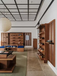 Modern Japanese-style entryway featuring warm teak wood open shelving for shoes, built-in blue cushioned seating, a large paper lantern pendant, and tatami-style green rugs on a stone tile floor.