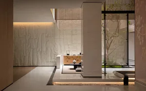 Modern Japanese minimalist tea room featuring a large textured limestone wall, warm cove lighting, wooden console with tea set, and direct view to a lush green courtyard garden through floor-to-ceiling glass.