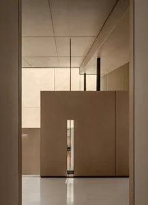 Modern minimalist hallway featuring large oak wood panels, white marble floor, high ceiling with recessed lighting, and a narrow vertical opening revealing a hidden passage.
