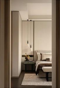 View into a modern minimalist bedroom with beige textured walls, two white pendant lights, a sage green bedside table, and a bed dressed in neutral and brown linens.