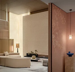 Modern luxury living room featuring a large curved cream bouclé sofa, textured beige wall panels, a dramatic blush pink accent wall with floral pattern, marble floor, and warm ambient lighting.