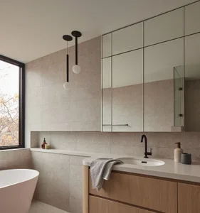 Modern minimalist bathroom with large-format travertine tile walls, floating light oak vanity with white countertop, black matte faucet, integrated mirror cabinet, and two black pendant lights with white glass globes above a freestanding white bathtub.