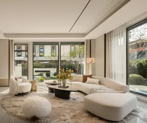 Modern minimalist living room featuring a large curved white boucle sofa, matching ottoman, white fur pouf, black coffee table, and floor-to-ceiling windows overlooking a lush garden.