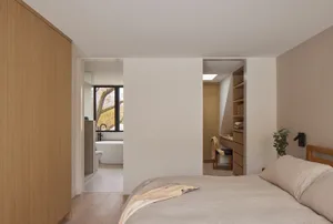 Modern minimalist bedroom with light oak wardrobe and bed, opening directly to a white ensuite bathroom with freestanding bathtub and large window.