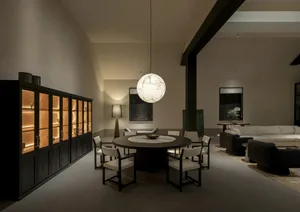 Modern open-plan dining and living area featuring a large round dark wood dining table, six white upholstered chairs, a dramatic white marble sphere pendant light, and dark wood illuminated display cabinet.