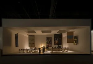 Modern art gallery exhibition booth with minimalist wooden furniture, hanging fabric banners, and warm spotlighting in a dark hall