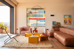 Bright modern living room featuring a terracotta leather sofa and armchair, bold yellow nesting tables, a large colorful abstract painting, and a patterned area rug with an arched floor lamp.