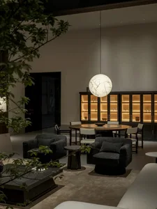 現代奢華客餐廳空間，設有深色泡泡紗旋轉扶手椅、巨型球形吊燈、圓形木製餐桌，以及帶有暖光的深色木質展示櫃。