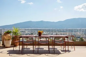 Outdoor dining table and six chairs in terracotta color on a rooftop terrace overlooking a vast mountain range and cityscape