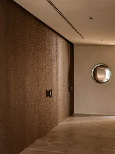 Modern minimalist hallway featuring a heavily textured brown wall, large-format travertine stone floor, and a round convex mirror on a neutral wall.