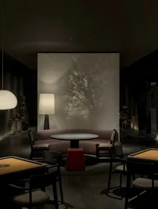 Luxurious modern game lounge featuring a curved textured sofa, round black table, dramatic tree shadow projection on a backlit wall, and warm ambient lighting.