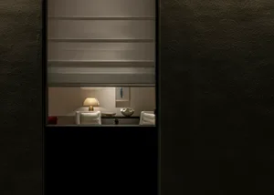 View through a dark textured wall opening into a warmly lit private lounge featuring white armchairs, a table lamp, and decorative objects.
