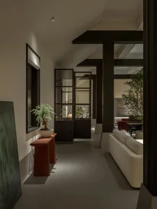 Modern minimalist hallway featuring dark wood structural beams, a white sectional sofa, terracotta console table with bonsai tree, and large green artwork.