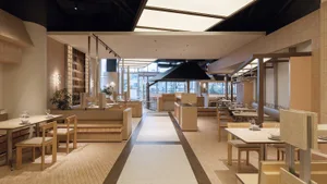 Modern Japanese restaurant interior featuring light wood banquette seating, stone-topped tables, and a long central aisle with skylight illumination.