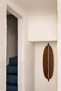 View of a modern staircase with dark blue steps through a textured white plaster opening, featuring an oval walnut wall sconce with vertical light on the right wall.