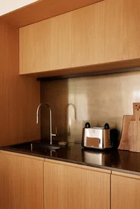 Close-up of a modern kitchen counter in light oak with a black sink, brushed metal faucet, stainless steel toaster, and metallic backsplash.