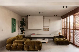 Modern minimalist living room featuring two olive green modular velvet sofas, a stone coffee table, concrete walls and ceiling, wooden window shutters, and a large potted fiddle leaf fig tree.