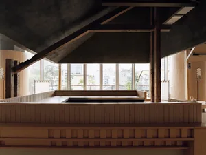 Modern Japanese-style tea room featuring a sunken tatami platform made of light hinoki wood, dark concrete ceiling with exposed heavy timber beams, large city-view windows, and warm vertical wood paneling.