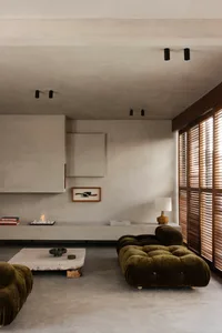 Modern minimalist living room with olive green velvet tufted cloud sofa, raw concrete walls, floating console, and stone coffee table.
