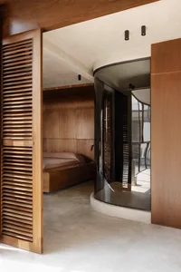 Modern minimalist bedroom featuring rich walnut wood paneling, a platform bed, and a distinctive curved glass partition wall with black frame.