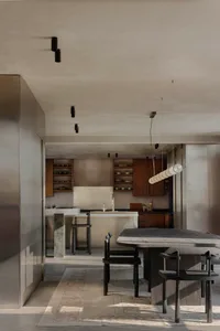 Modern minimalist open-plan kitchen and dining area featuring a dark walnut dining table, matching wooden chairs, concrete kitchen island, and warm walnut cabinetry under a sculptural cylindrical pendant light.