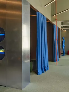 Modern retail fitting room with brushed stainless steel cabinetry, circular display cutouts showing sneakers, royal blue privacy curtains, and a blue mannequin in the background.