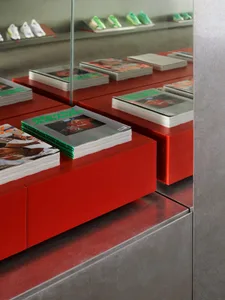 Close-up view of stacked magazines on glossy bright red lacquered display blocks with mirrored background reflecting sneakers.