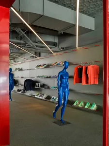 Interior view of a contemporary sportswear store featuring bright blue glossy mannequins, wall-mounted display shelves with colorful sneakers, hanging athletic apparel, and dramatic linear LED lighting.
